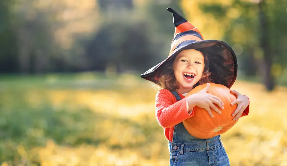 A child wearing a witch hat holding a pumpkin